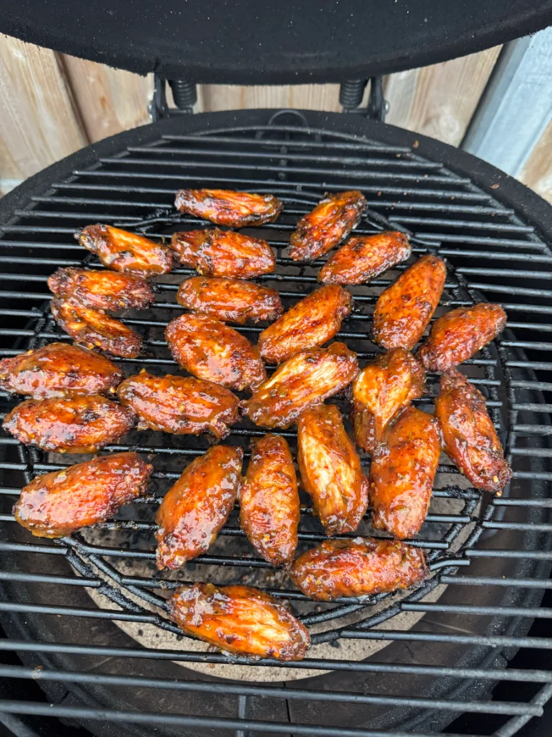 Gekruide kippenvleugels met een donkerrode rub op het rooster van een kamado